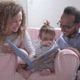 young adoptive mother and father read a book with toddler girl