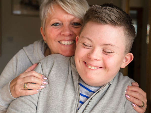 adoptive mother hugs her smiling son who has special needs