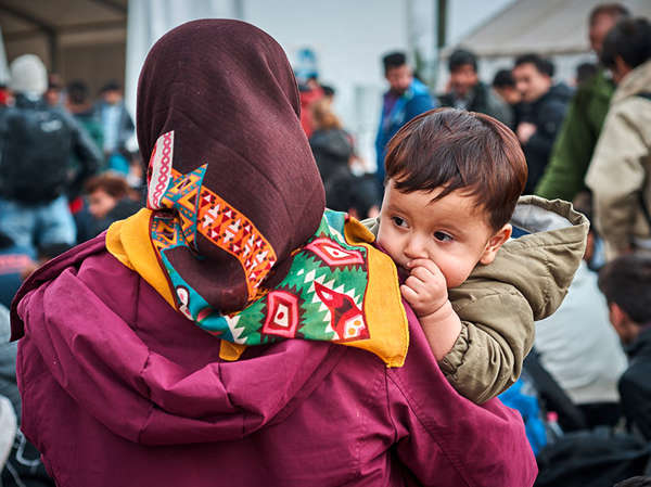Latin American woman holds her young son as they walk through a refugee camp