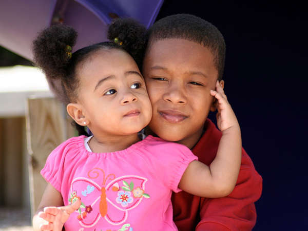 an african american teenage boy hugs his toddler sister in their foster parents' home