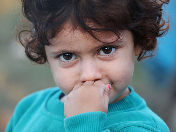 Young curly-haired girl holds her hand to her face with a serious expression