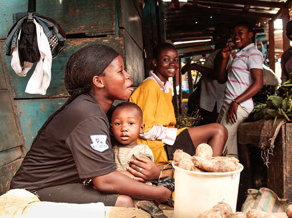 A Ghanaian mother hugs her young son while selling potatoes at the market