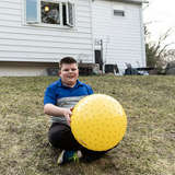 young boy in foster care plays with a large, yellow ball in the backyard
