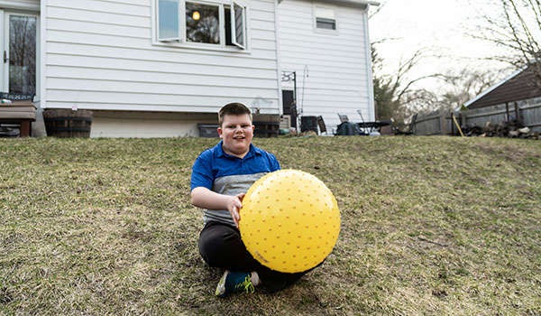 young boy in foster care plays with a large, yellow ball in the backyard