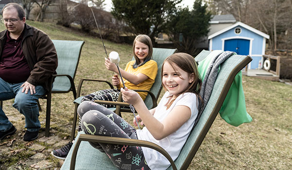 two girls roast marshmallows over a fire in the backyard of their adoptive parents' house