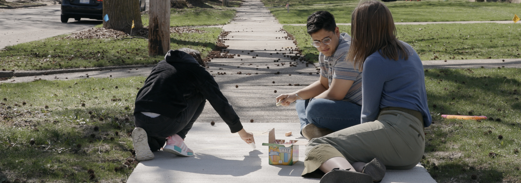 Young diverse married couple play with chalk on sidewalk with refugee girl