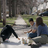 Young diverse married couple play with chalk on sidewalk with refugee girl