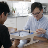 Foster dad plays a game at the kitchen table with Afghan refugee teenage boy