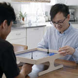 Foster dad plays a game at the kitchen table with Afghan refugee teenage boy