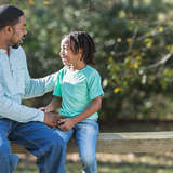 african american adoptive father speaks to his son on a park bench