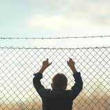 Young hispanic boy clings to fence with barbed wire