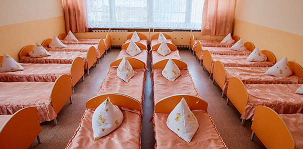 identical, small orange beds fill a room at an orphanage