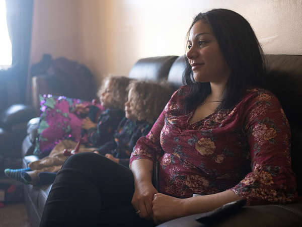 woman looks off into the distance while her two twin boys sit on the couch next to her
