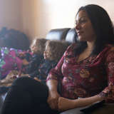 woman looks off into the distance while her two twin boys sit on the couch next to her