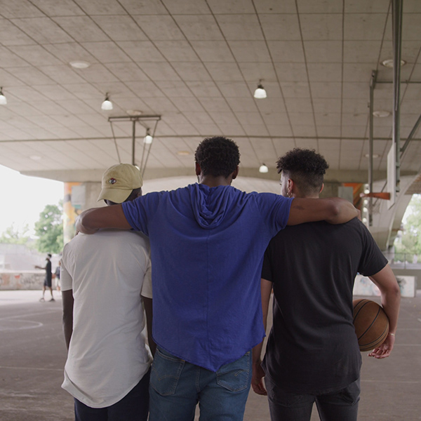 Black foster father puts his arm around two Black teenagers playing basketball