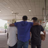 Black foster father puts his arm around two Black teenagers playing basketball