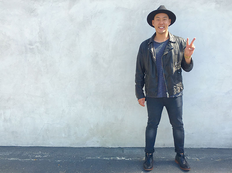 young asian adult adoptee holds up the peace sign in front of a concrete wall