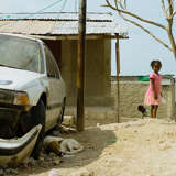 young Haitian girl looks at the wreckage of a car after the hurricane