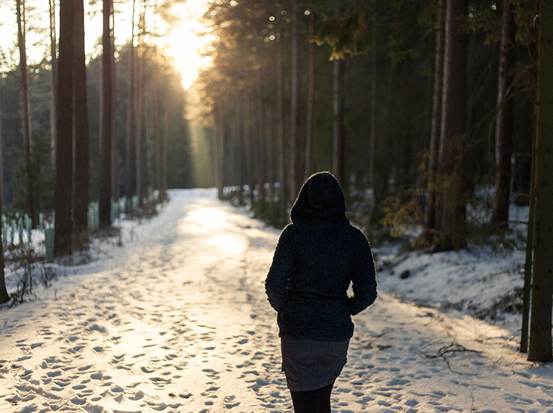 young woman walks along a snowy path at sunset