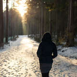 young woman walks along a snowy path at sunset