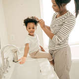 african american mother does her daughter's hair in the bathroom