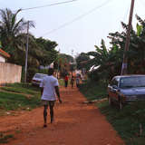 Young Ghanaian teen walks down dirt path in rural town.